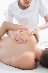 Professional female therapist giving shoulder massage to man in